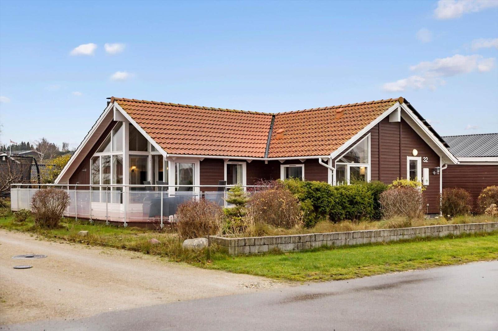 A house with brown cladding and red roof. It has large windows and a terrace.