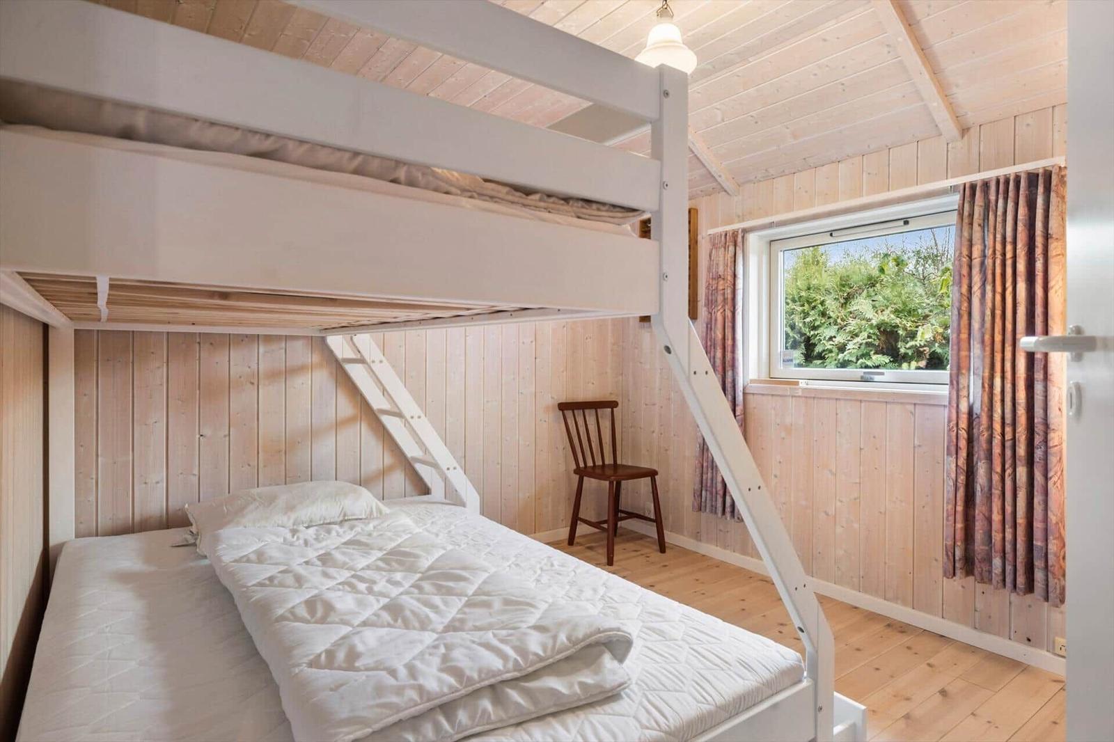 Room with bunk bed, wooden walls, and window with view of greenery.