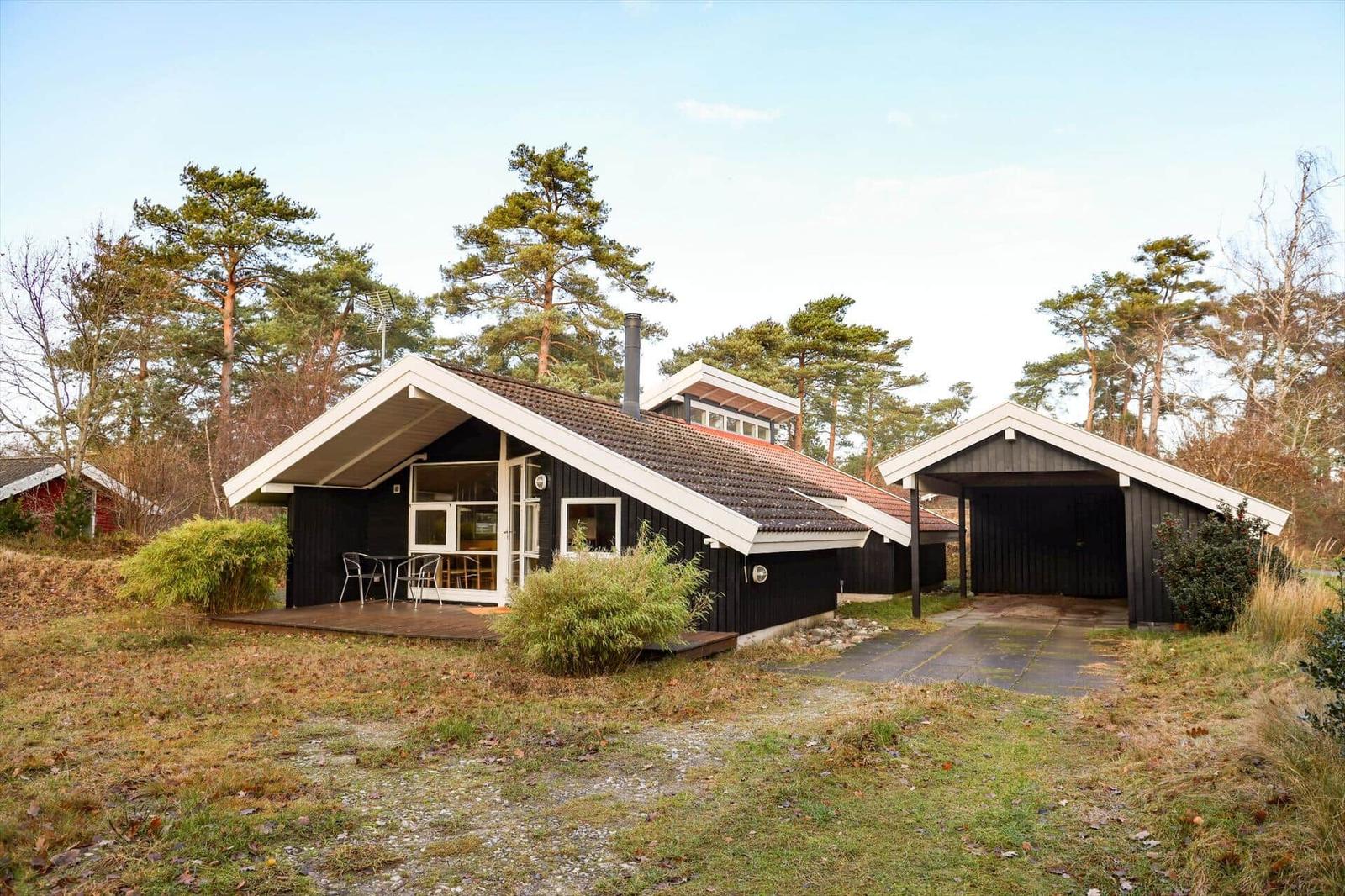 Black wooden house with terrace and garage in forest area.
