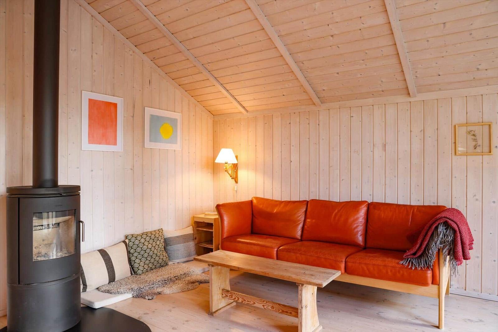 Living room with wooden walls, red sofa, stove, and wooden table.