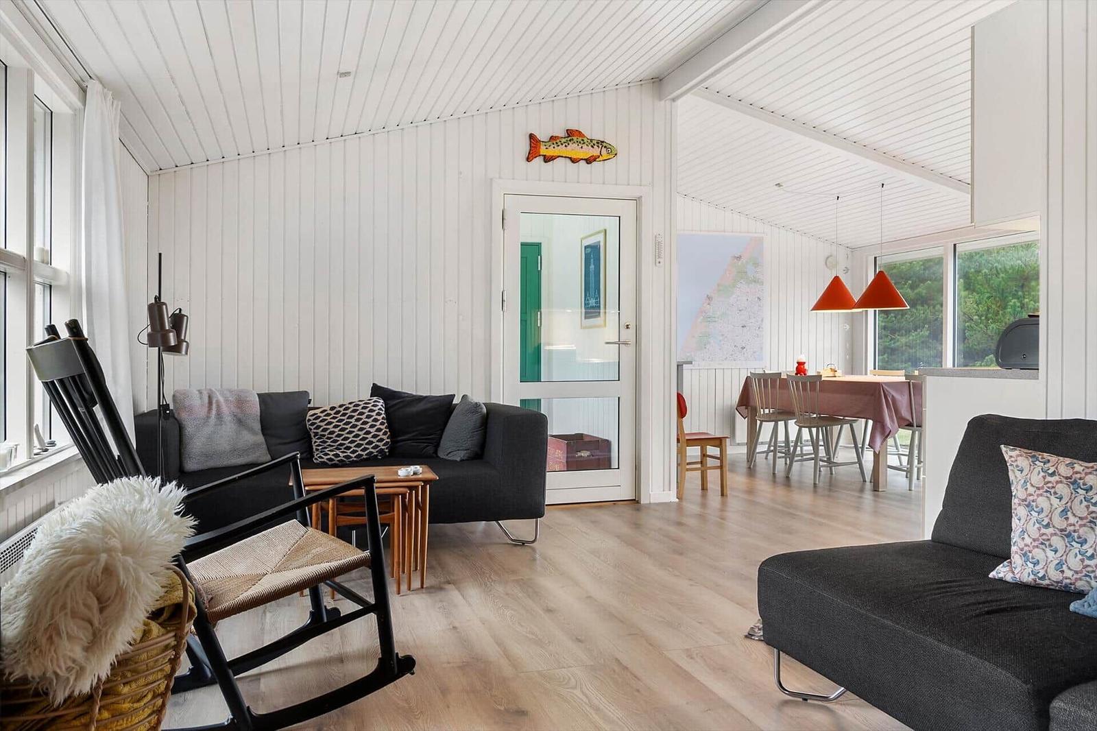 Wohn- und Essbereich mit schwarzen Sofas, Holzboden und weißem Paneelwandverkleidung.
