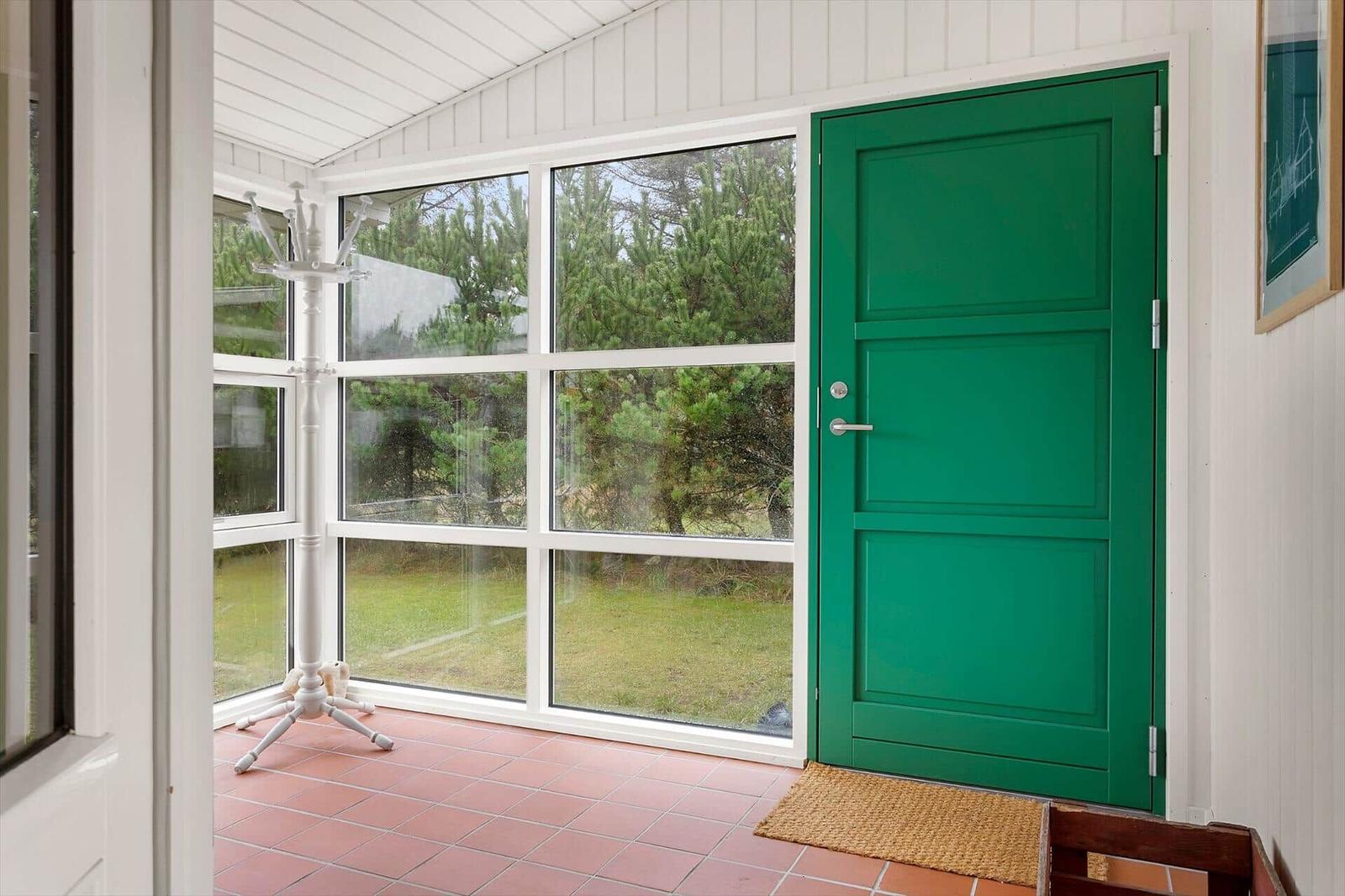 Eingangsbereich mit grüner Tür, großem Fenster und Terrakottboden.