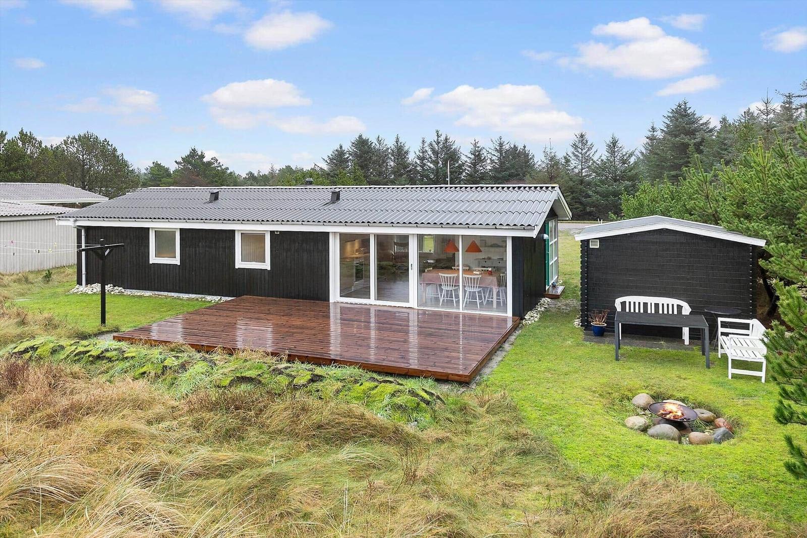 Ein Haus mit Terrasse, Grillplatz und Garten. Im Inneren ist eine Küche und Essbereich sichtbar.