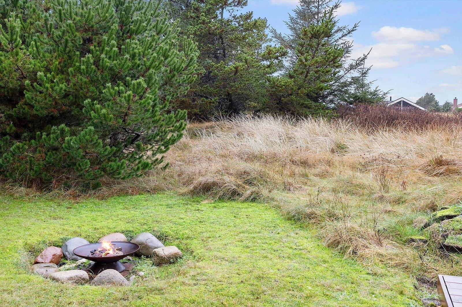 Feuerkorb mit Steinen im Garten unter Bäumen und Gras.