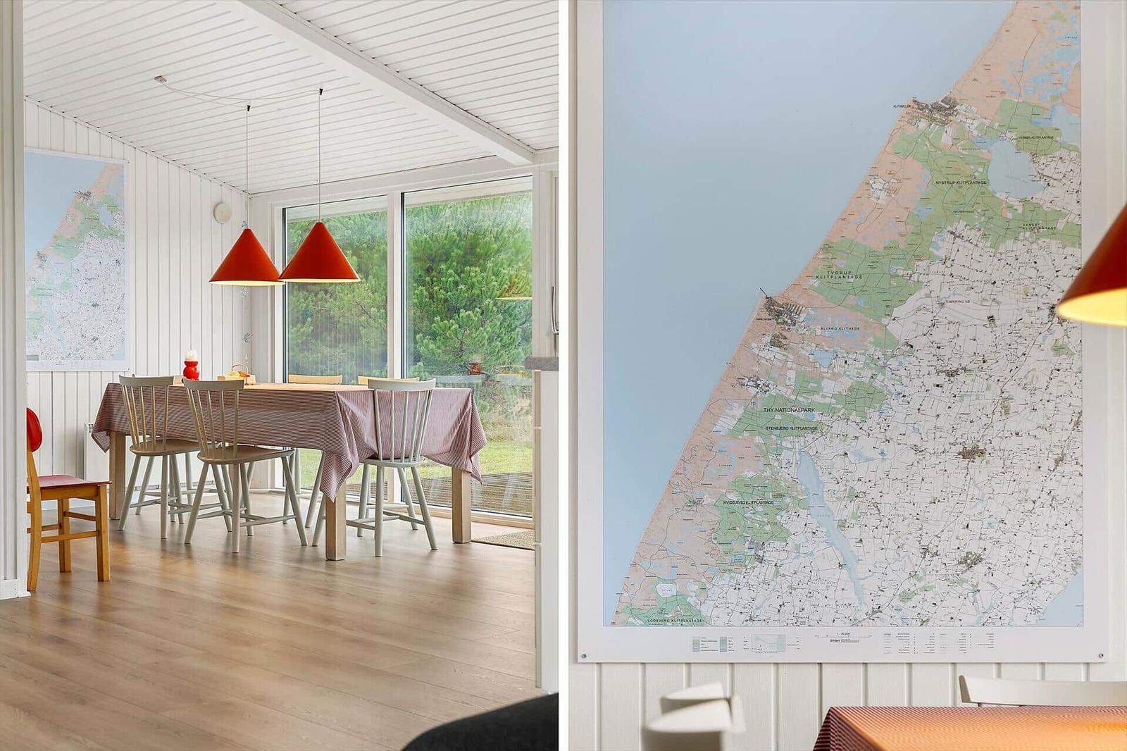 Esszimmer mit Tisch, Stühlen und großen Fenstern. Wandkarte zeigt Küstenregion.