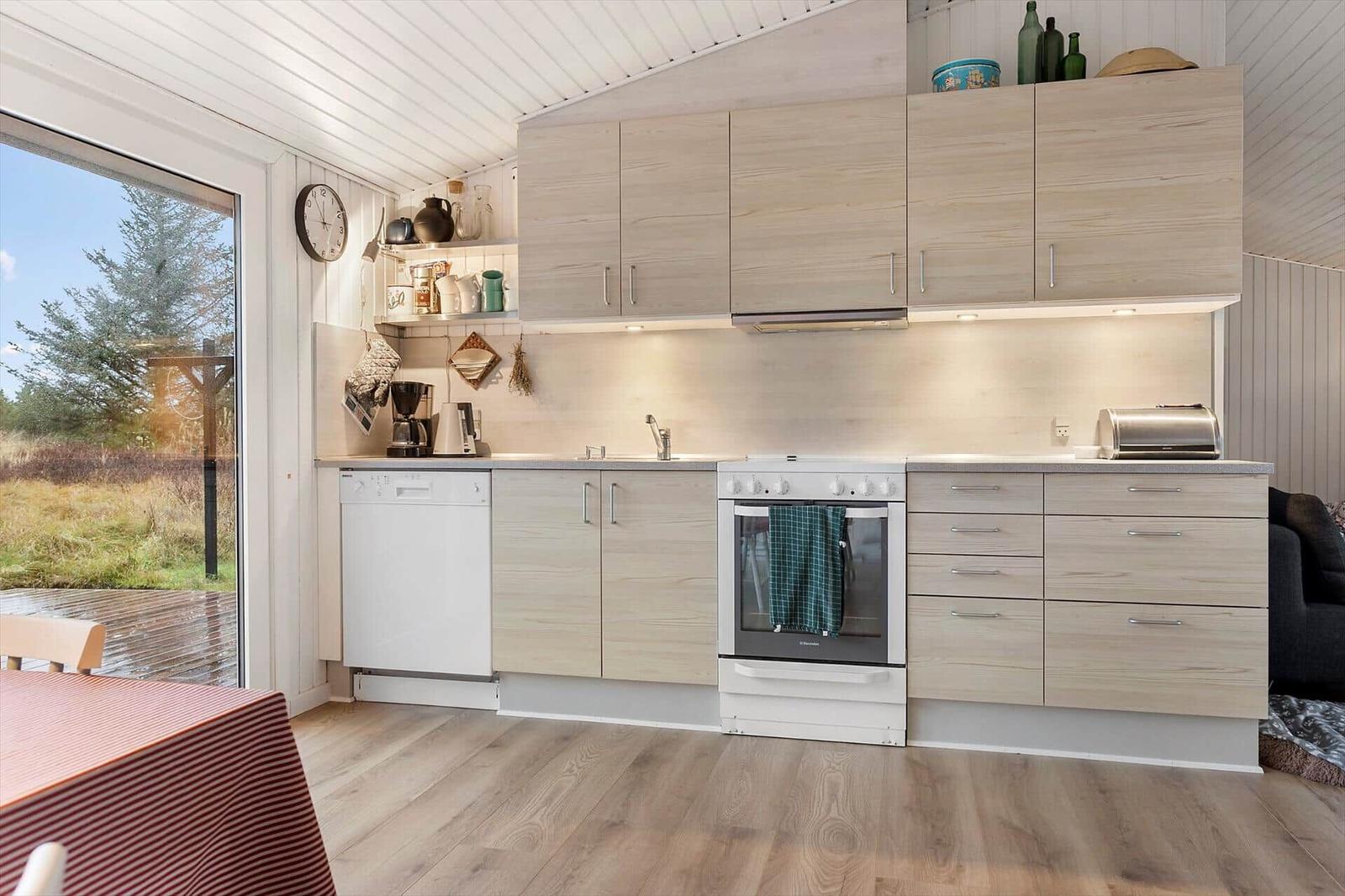 Küche mit Holzschrank, Spüle, Herd und Backofen. Durchgang zum Garten mit Holzterrasse.