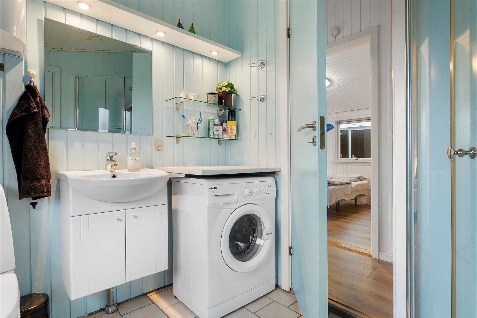 Badezimmer mit Waschmaschine, Spiegelschrank und Glasregalen an hellblauen Wänden.