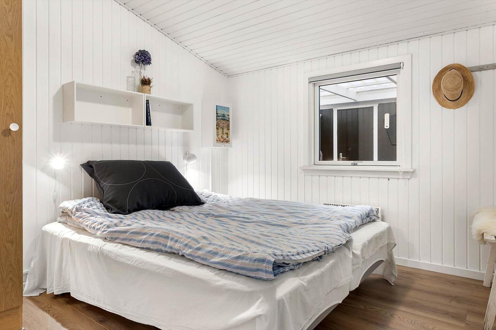 Schlafzimmer mit weiß verkleideten Wänden, Bett mit blau gemustertem Bettzeug und Fenster.