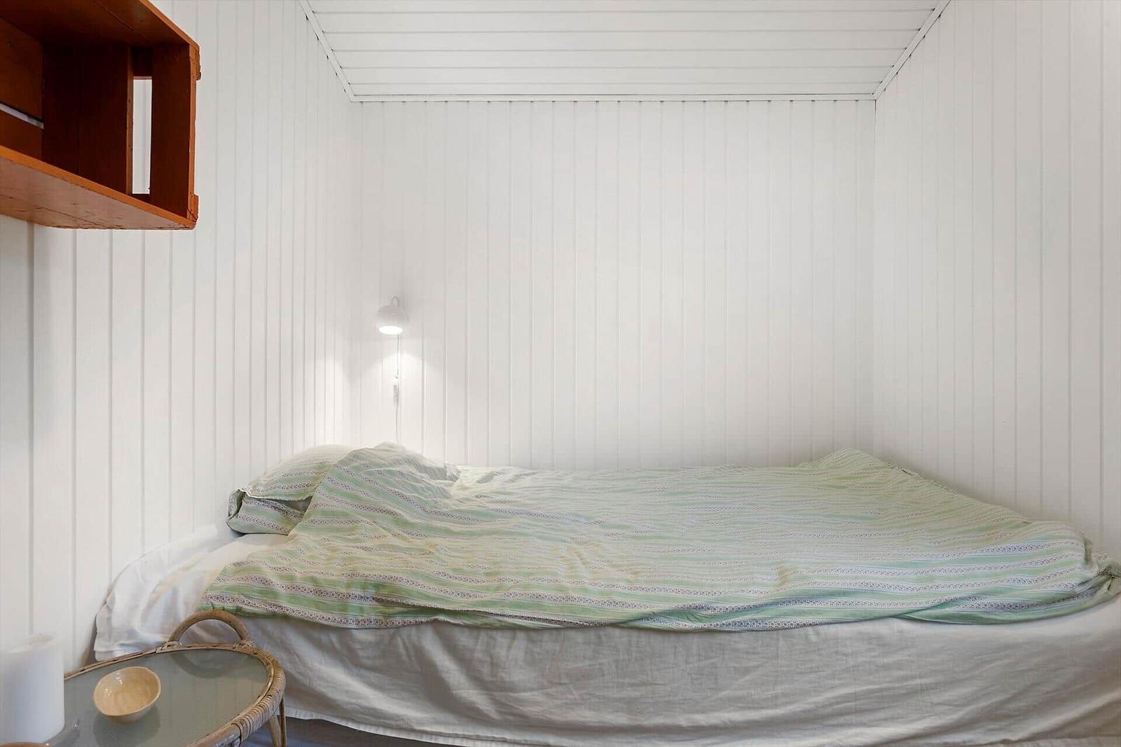 Schlafzimmer mit Bett, Wandlampe und Holzregal an der Wand.