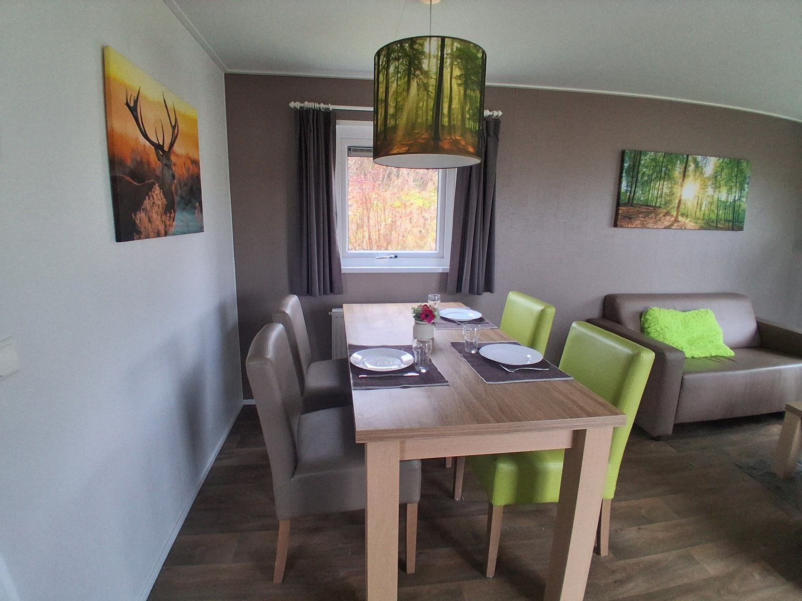 Essbereich mit Tisch, Stühlen und Sofa. Wandbilder und Fenster sichtbar.