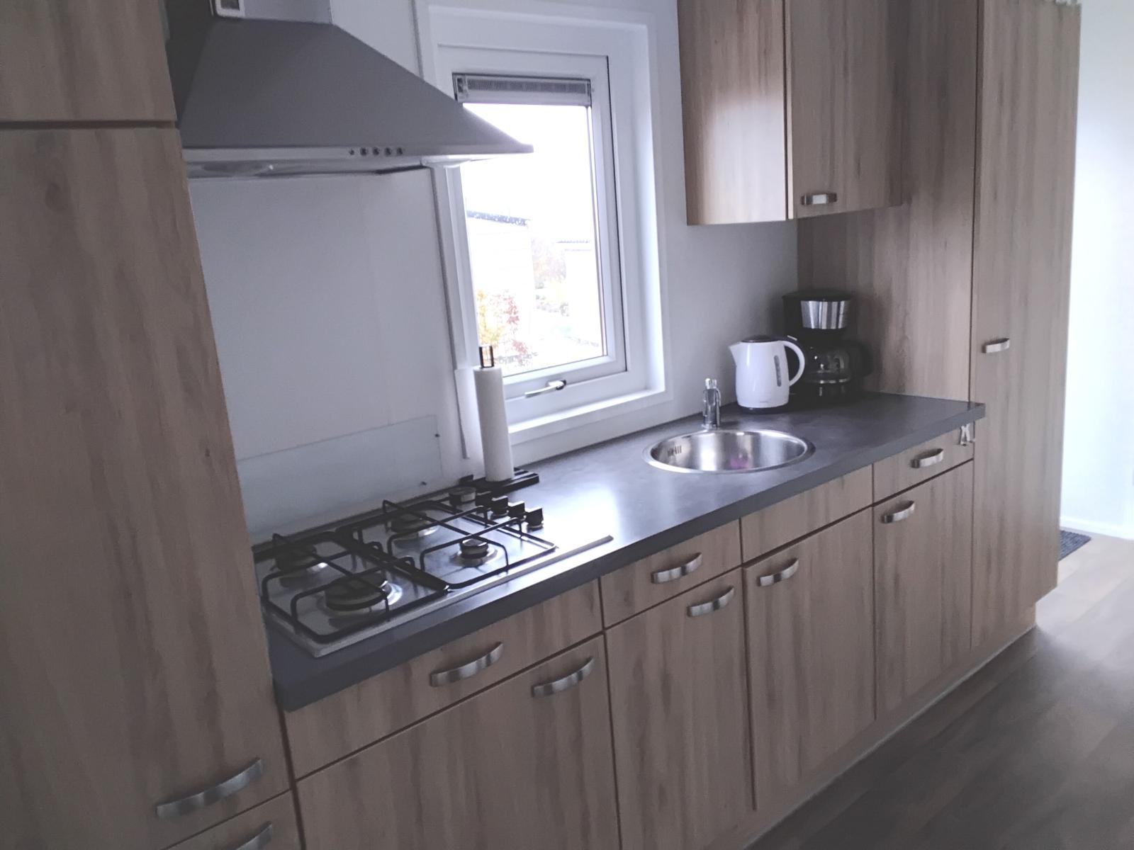 Küche mit Holzschränken, Herd, Spüle und Fenster.