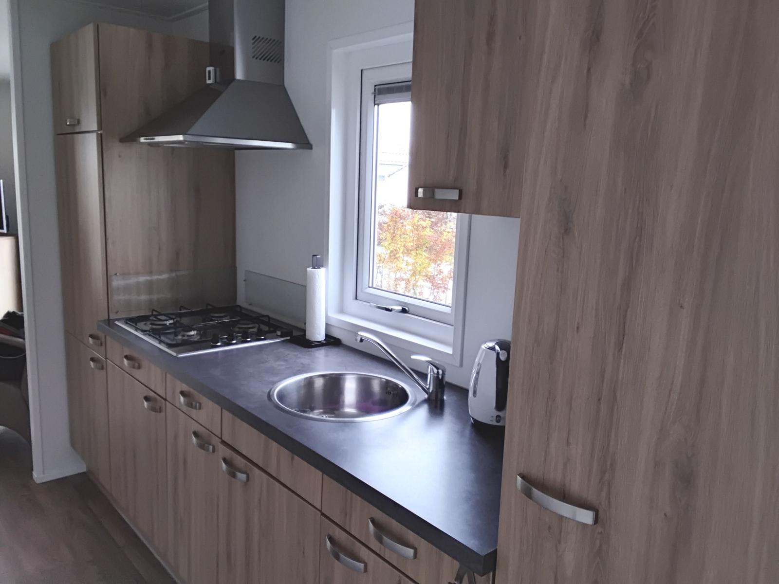 Küche mit Holzschränken, Herd, Spüle und Fenster.