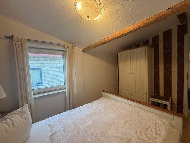 Schlafzimmer mit Bett, Fenster, Kleiderschrank und Holzbalken an der Decke.