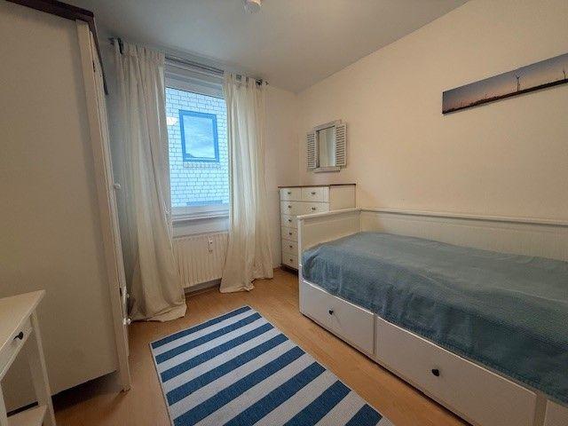 Schlafzimmer mit Bett, Schrank und Fenster mit Vorhängen.