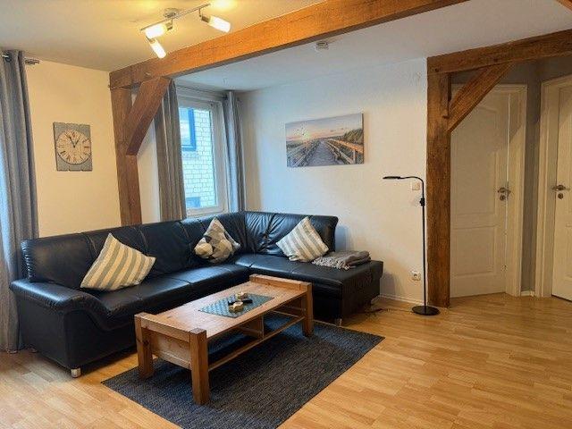 Wohnzimmer mit L-förmigem Sofa, Holzfußboden und Holzrahmen. Tisch und Teppich sind vorhanden.