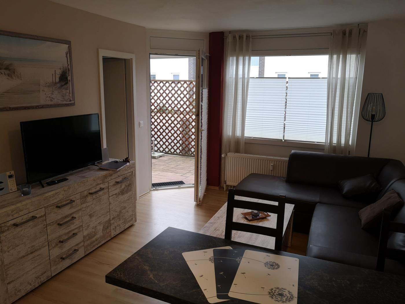 Wohnzimmer mit Sofa, TV und Terrasse. Fenster mit Jalousien.