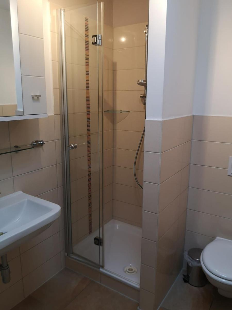 Bad mit Dusche, Waschbecken und Toilette. Fliesenwand und Spiegel.