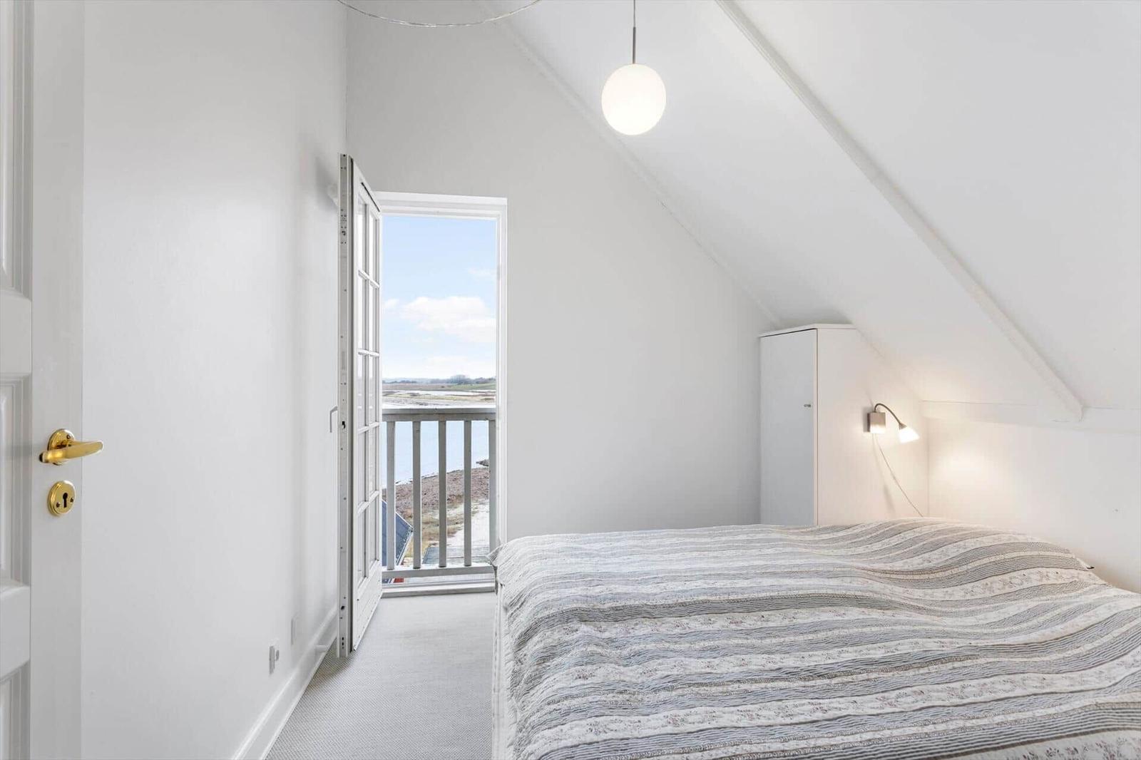 Bedroom with balcony, white furnishings, and sloped ceiling.