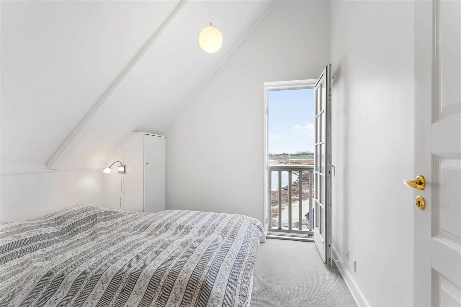 Bedroom with balcony view, white walls, and simple furnishings.