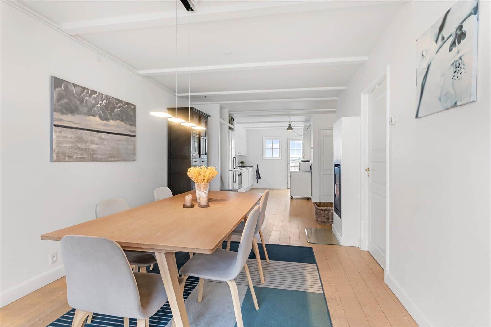 Dining room with wooden table, chairs, and view into the kitchen.