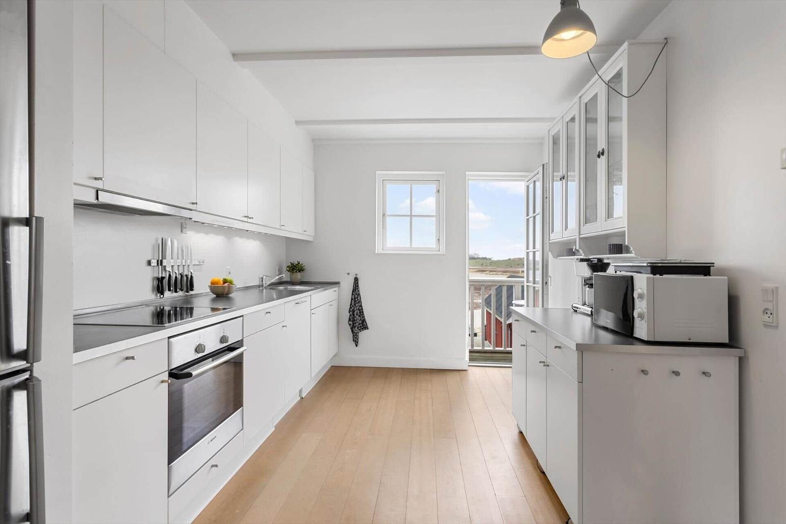 Kitchen with white cabinets, wooden floor, and view of balcony.