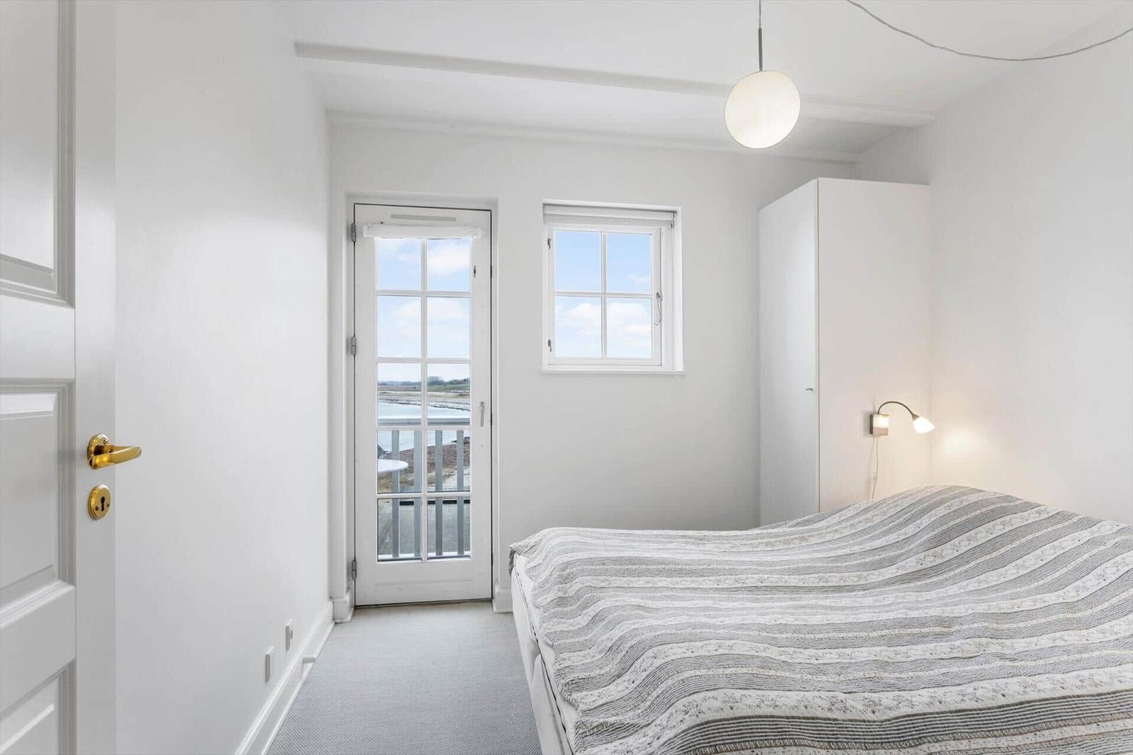 Bedroom with bed, windows, and door to balcony with water view.