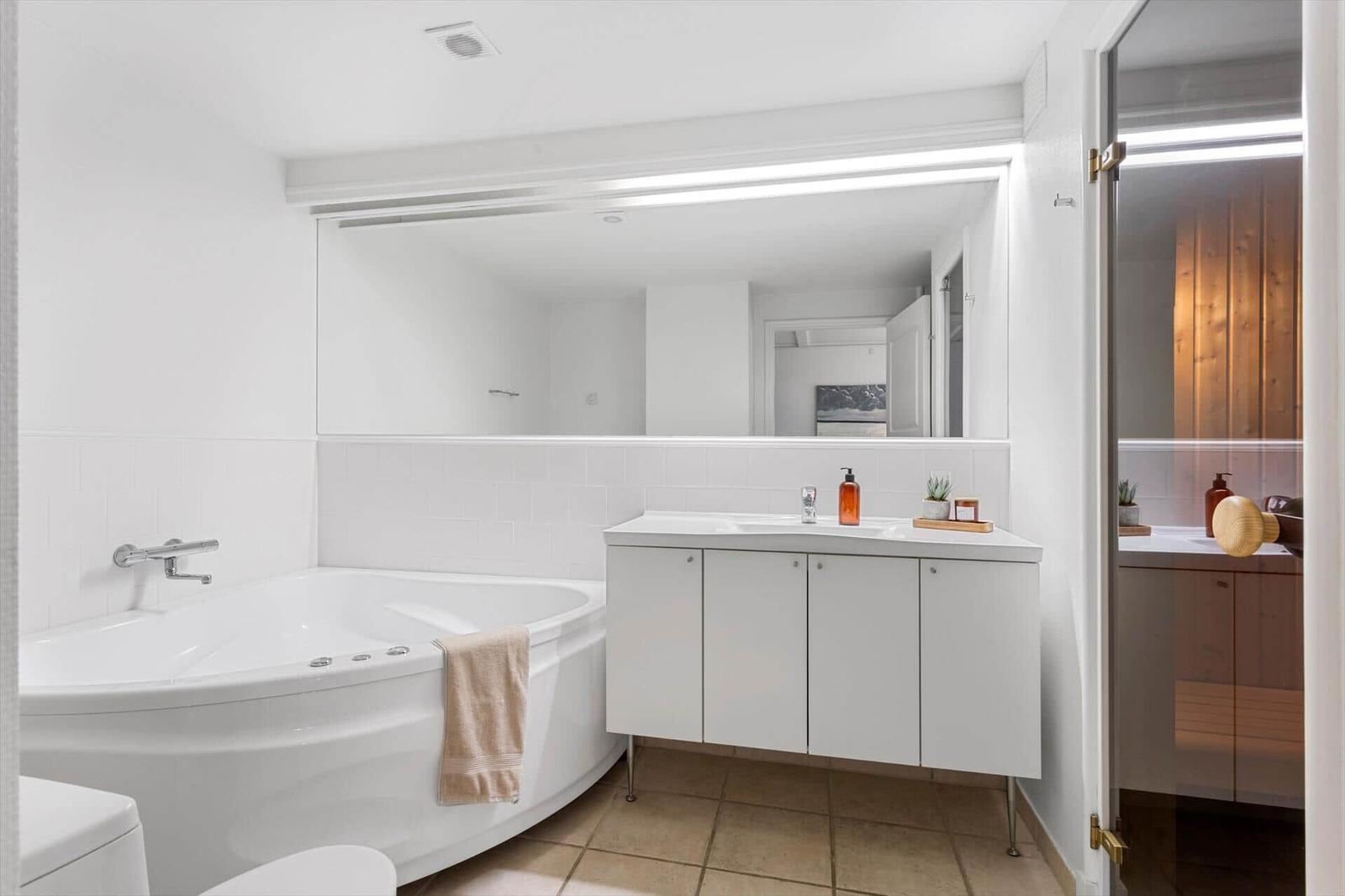 Bath with whirlpool, sink, and mirror. Entrance to sauna.