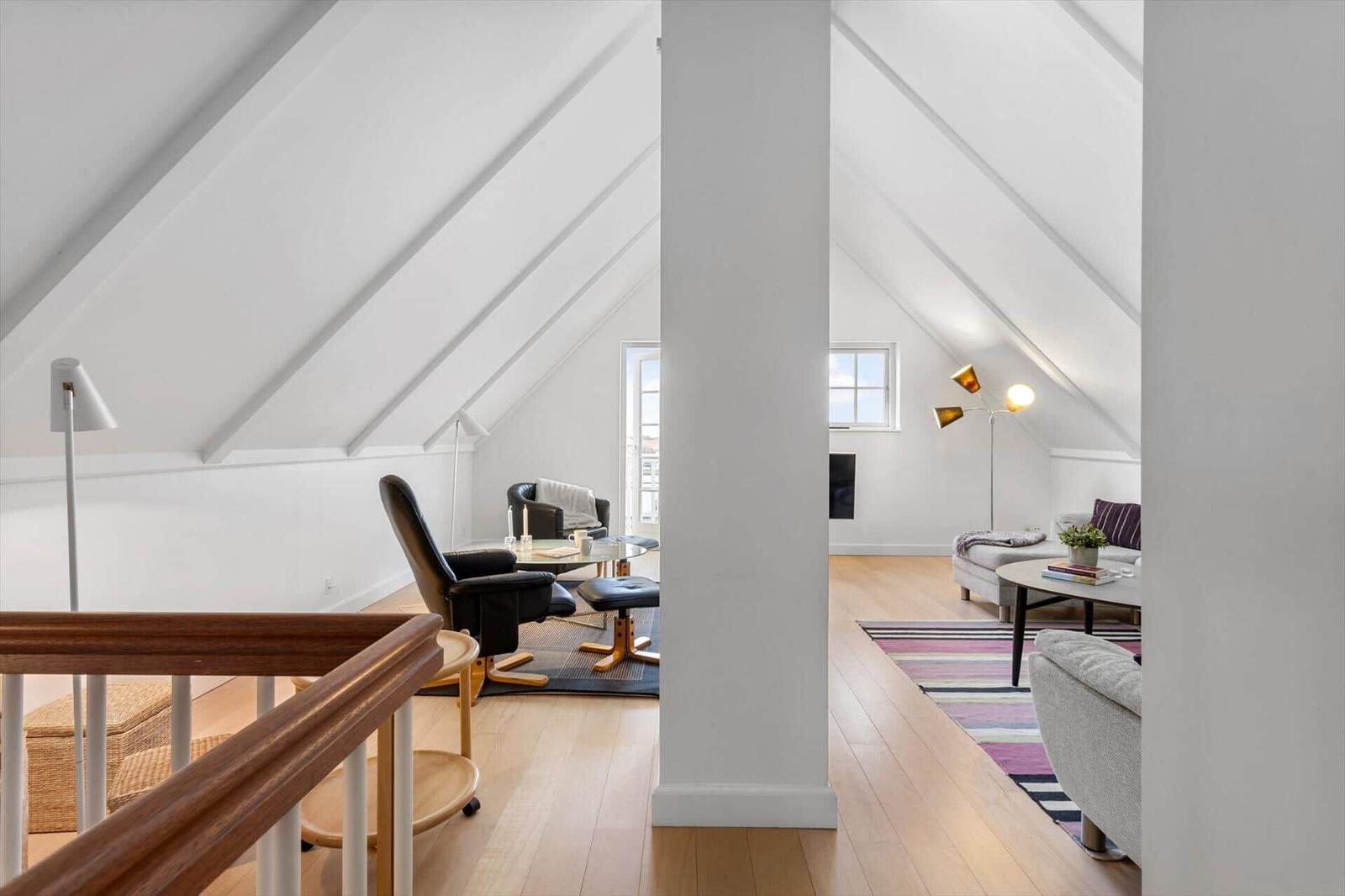 Attic apartment with wooden floor, seating areas, and windows.