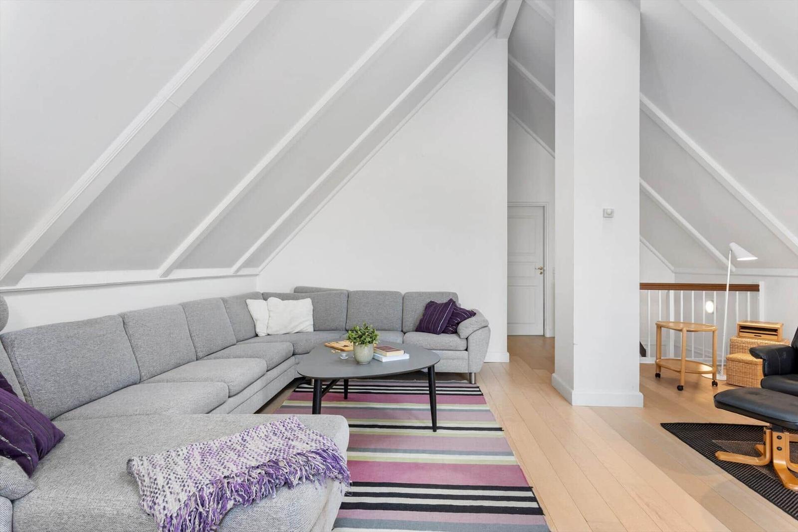 Living room with gray sofa, striped rug, and sloped ceiling beams.