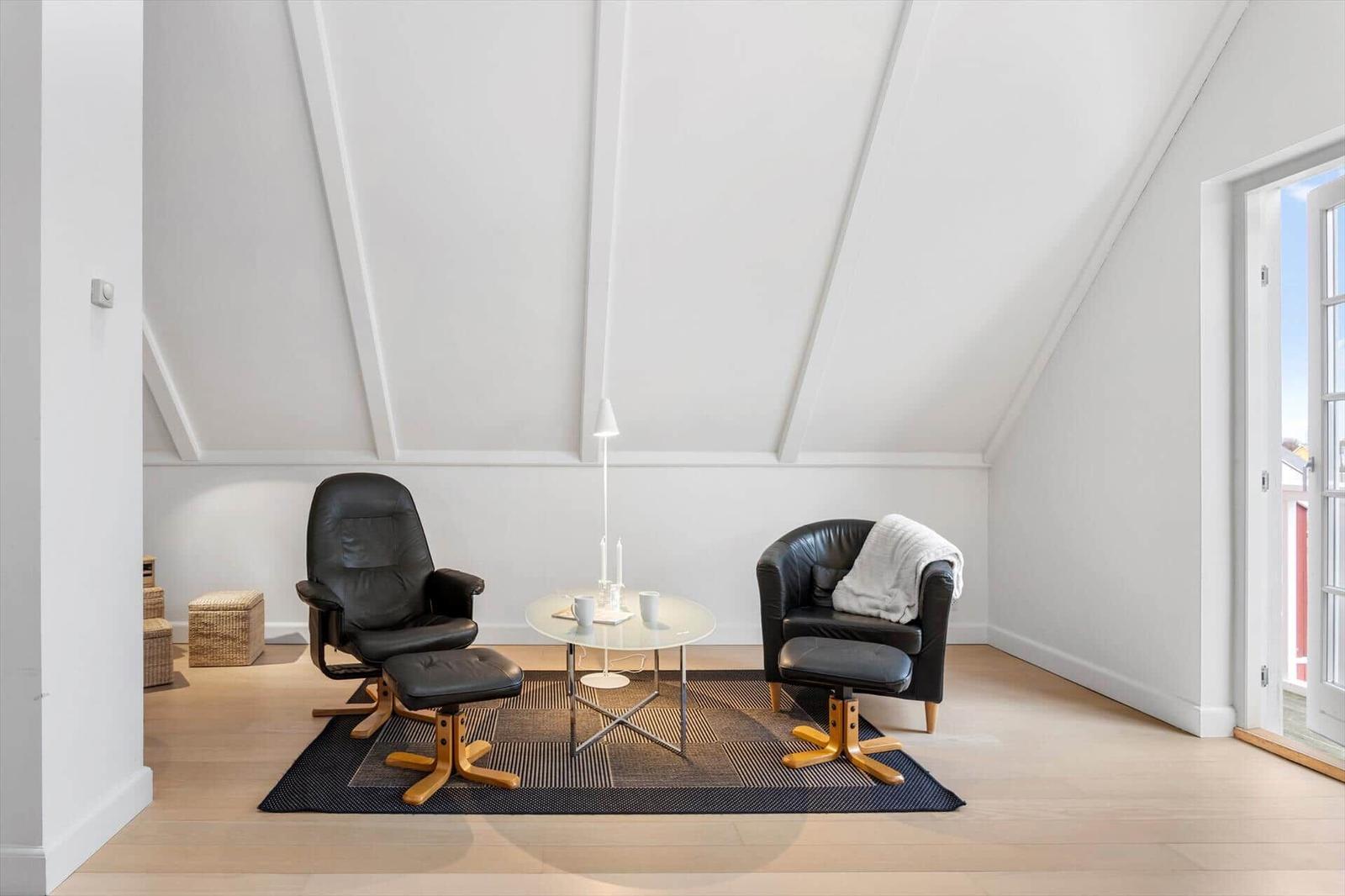 Two black leather chairs with wooden legs stand on a rug under a sloped ceiling.