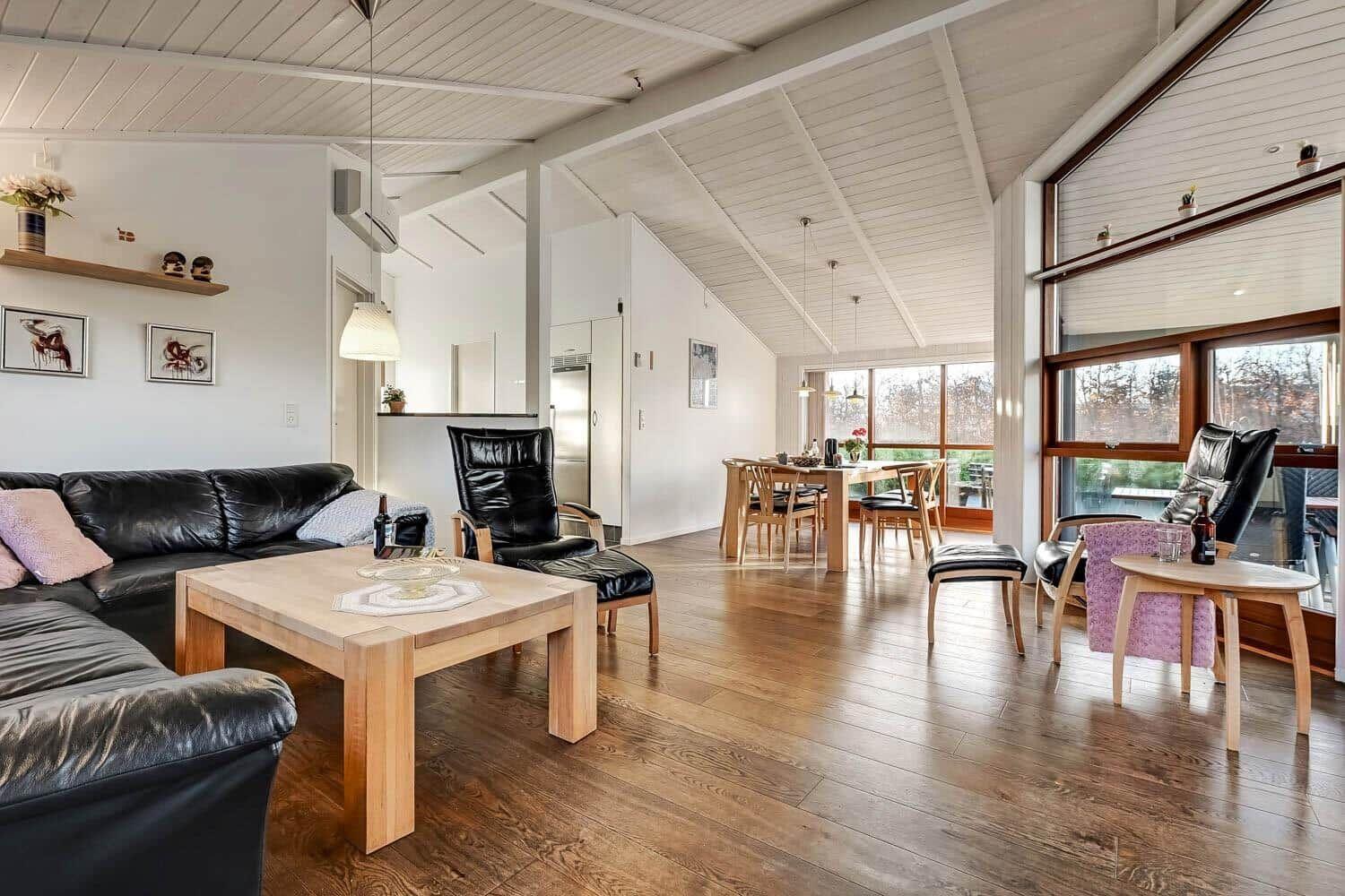 Living and dining area with hardwood floors, black leather furniture, and large windows.