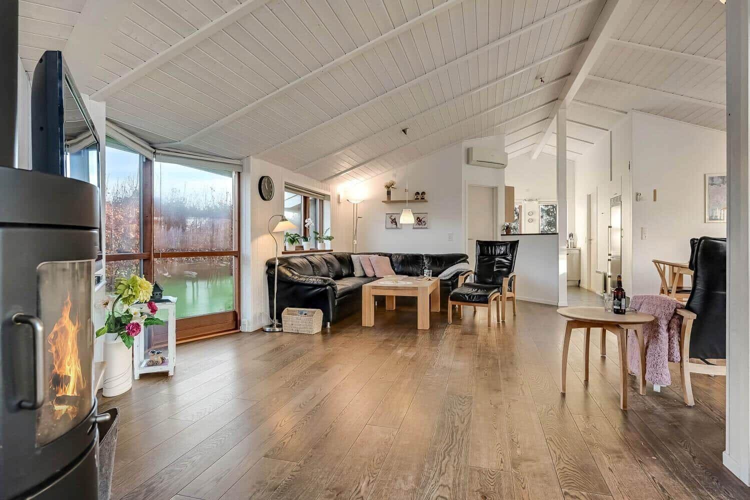 Living room with hardwood floor, sofa, chairs, and fireplace. Large windows with water view.