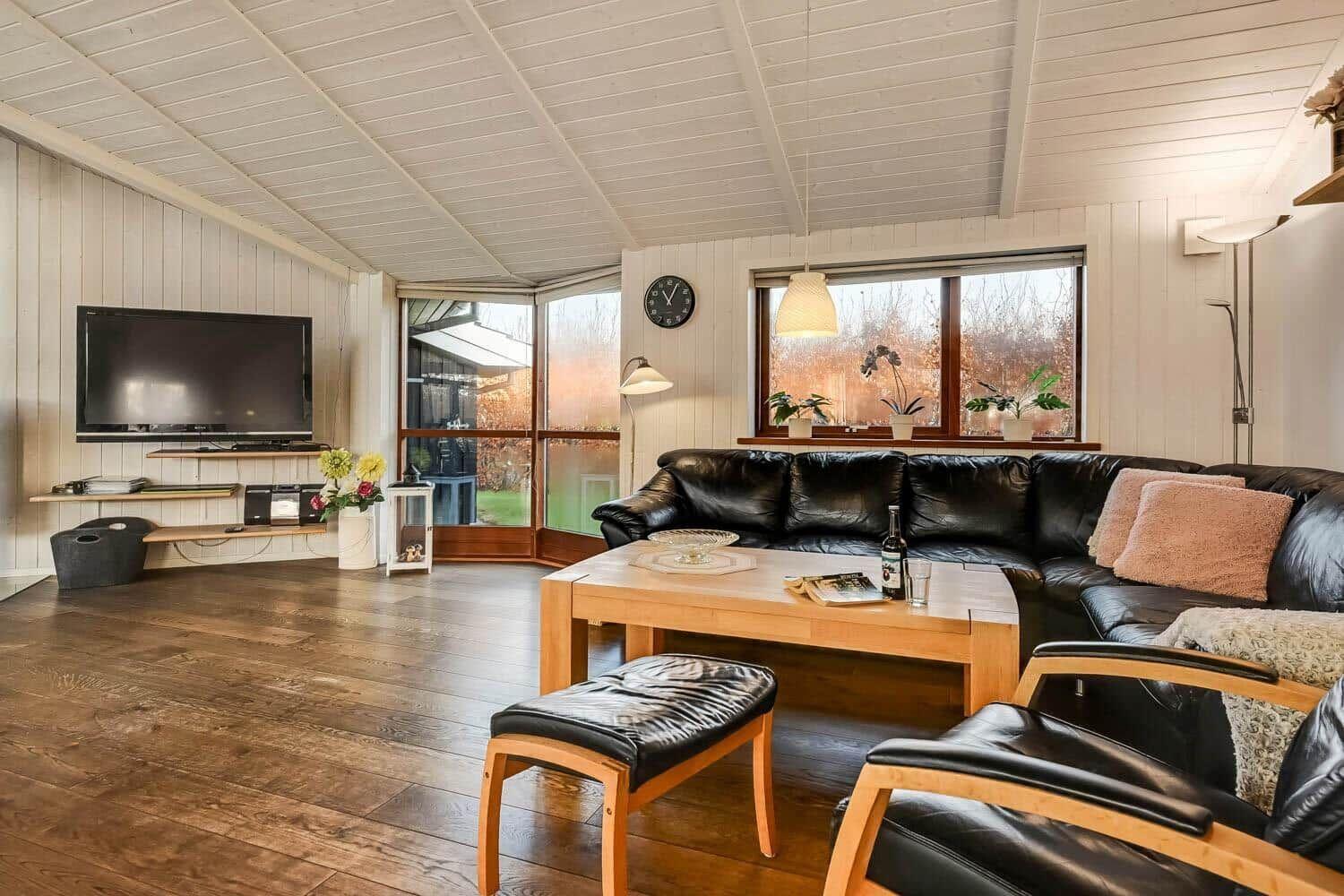 Living room with sofa, table, and TV. Wooden floor and large windows.