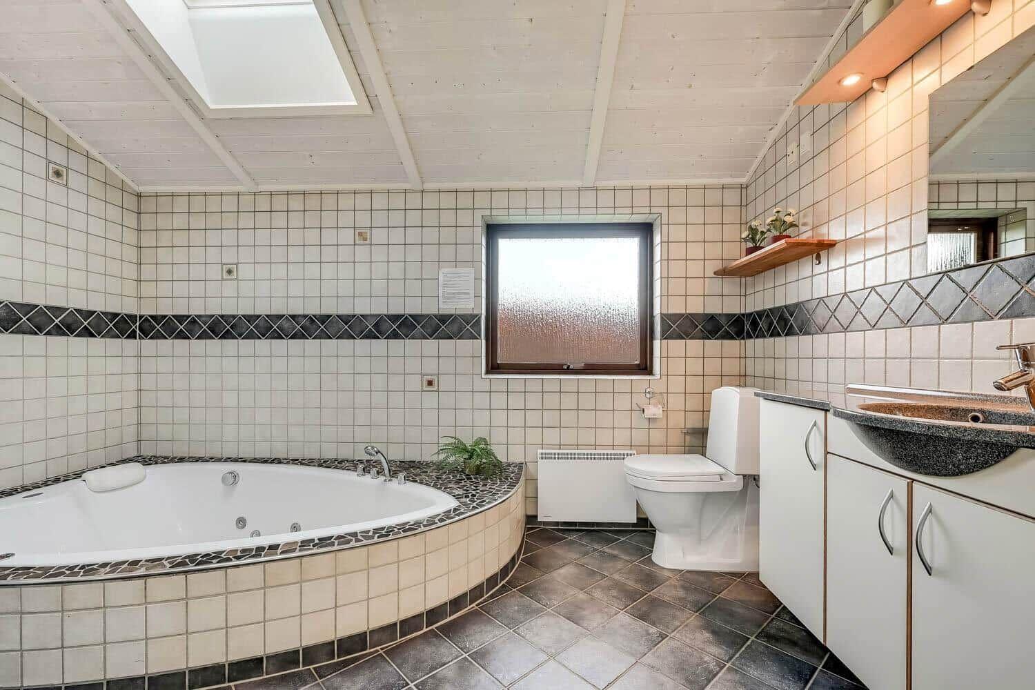 Bath with whirlpool, toilet, and sink. Window and skylight provide daylight.