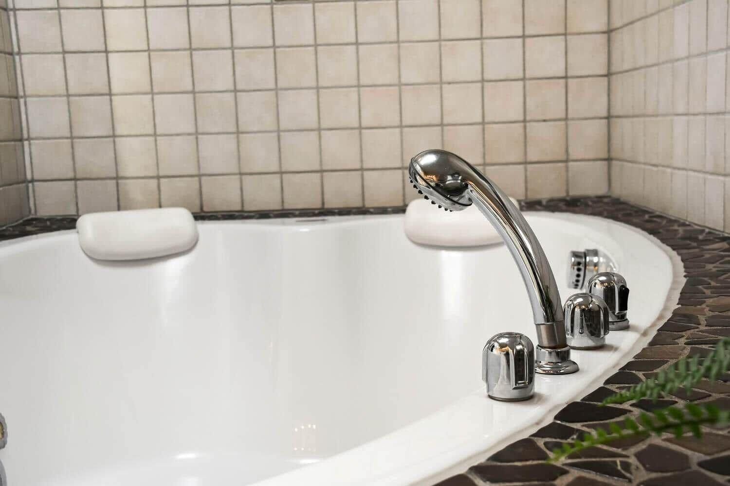 A bathtub with showerhead and faucets, surrounded by tiles and stone tiles.