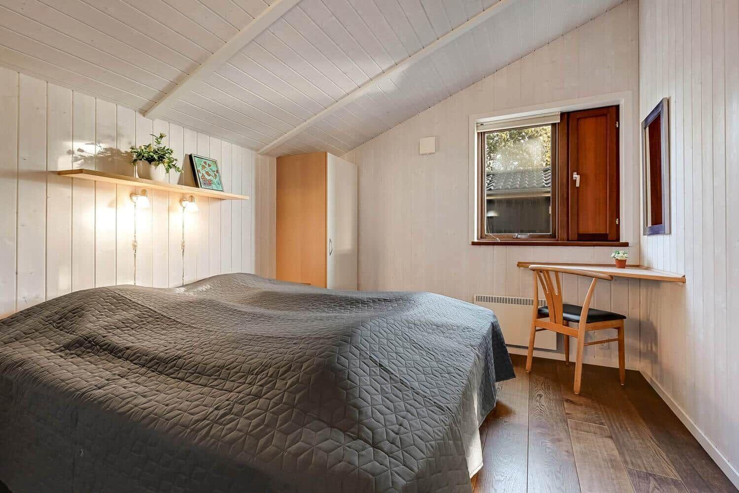 Bedroom with bed, desk, and window. Wooden walls and floor.