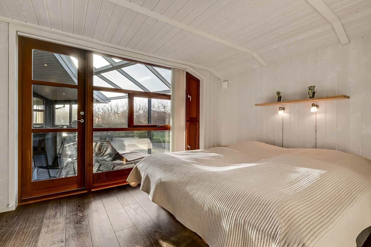 Bedroom with large bed, wooden floor, and floor-to-ceiling windows to terrace.