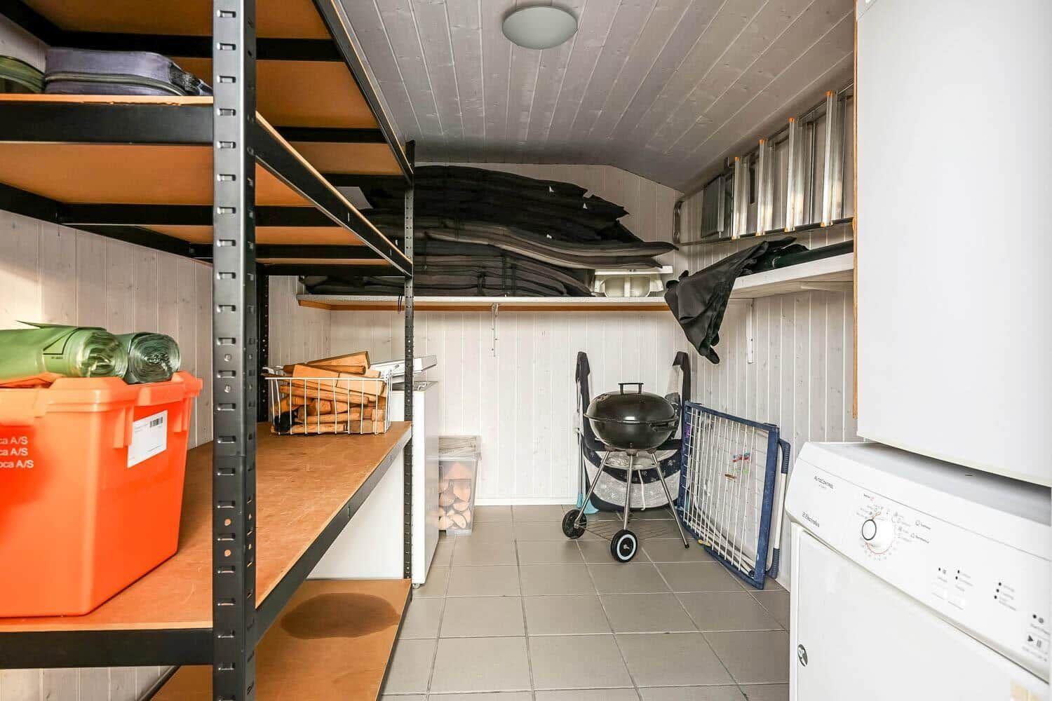 Vaulted room with shelves, grill, washing machine, and wood for fireplace.
