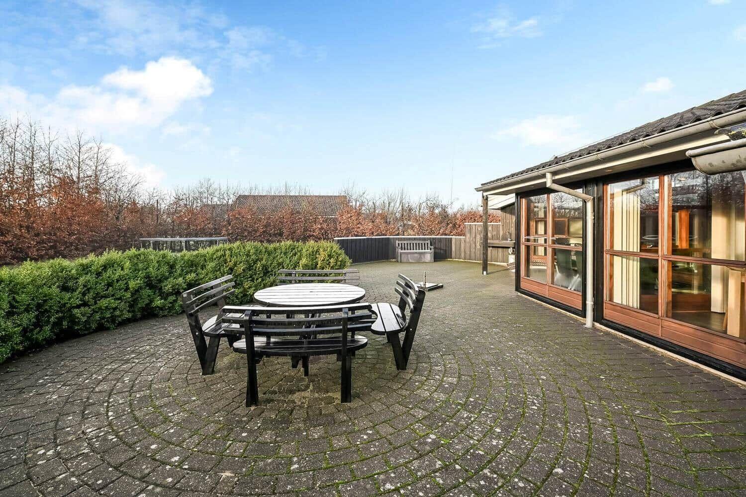 Terrace with table and chairs, paved, surrounded by hedge and garden.