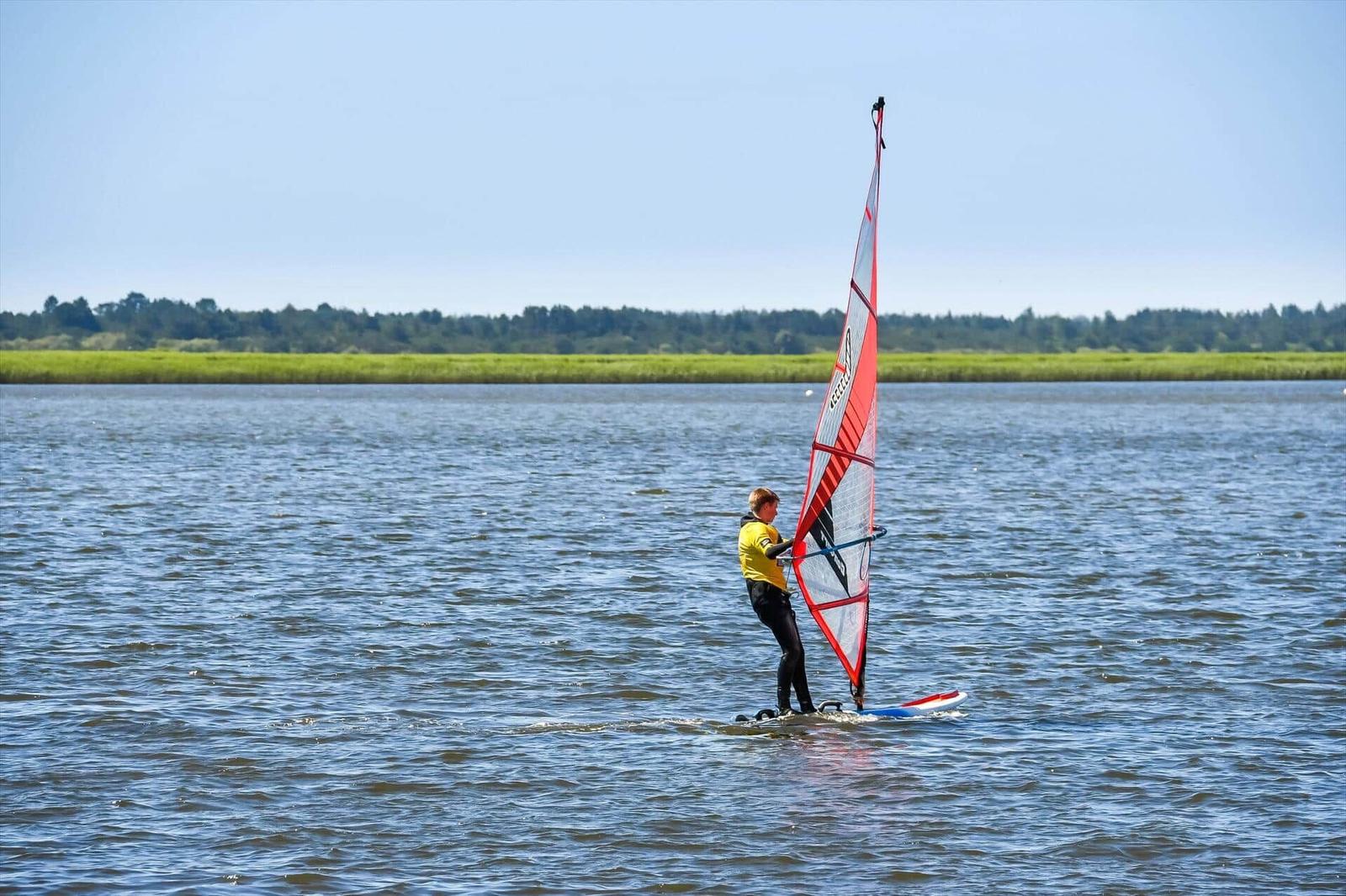 A windsurfer glides across calm waters with green land in the background.