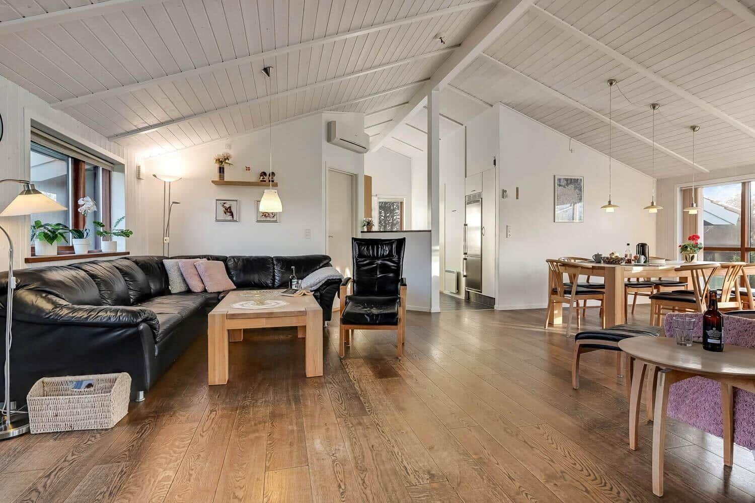 Living and dining area with wooden floor, black leather furniture, and dining table.
