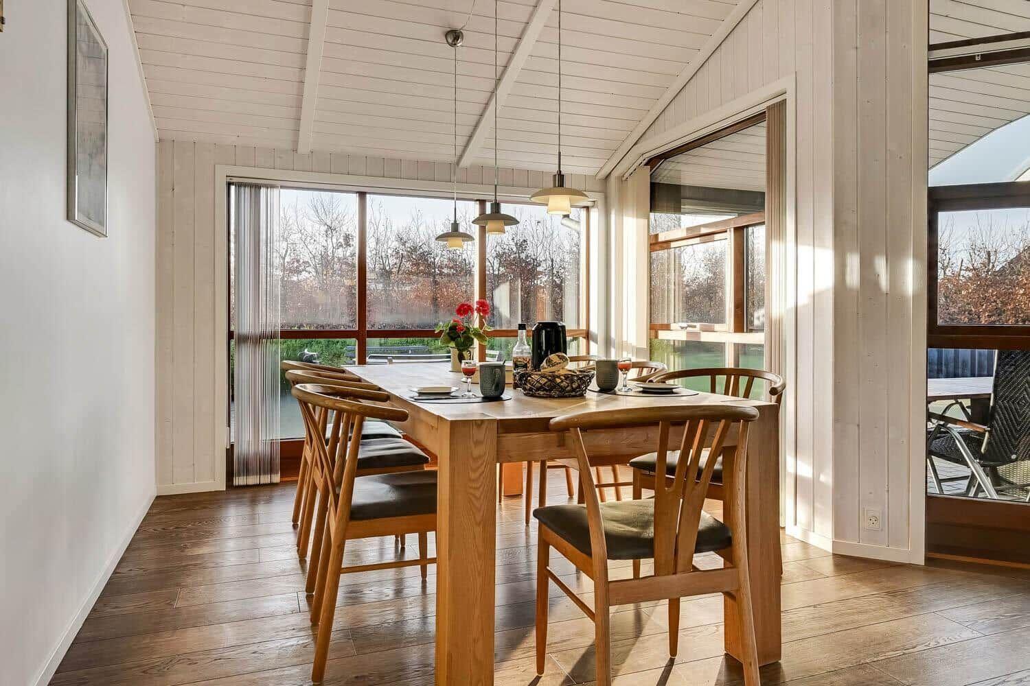 Dining room with wooden table, chairs, and large windows. Outside, a terrace is visible.