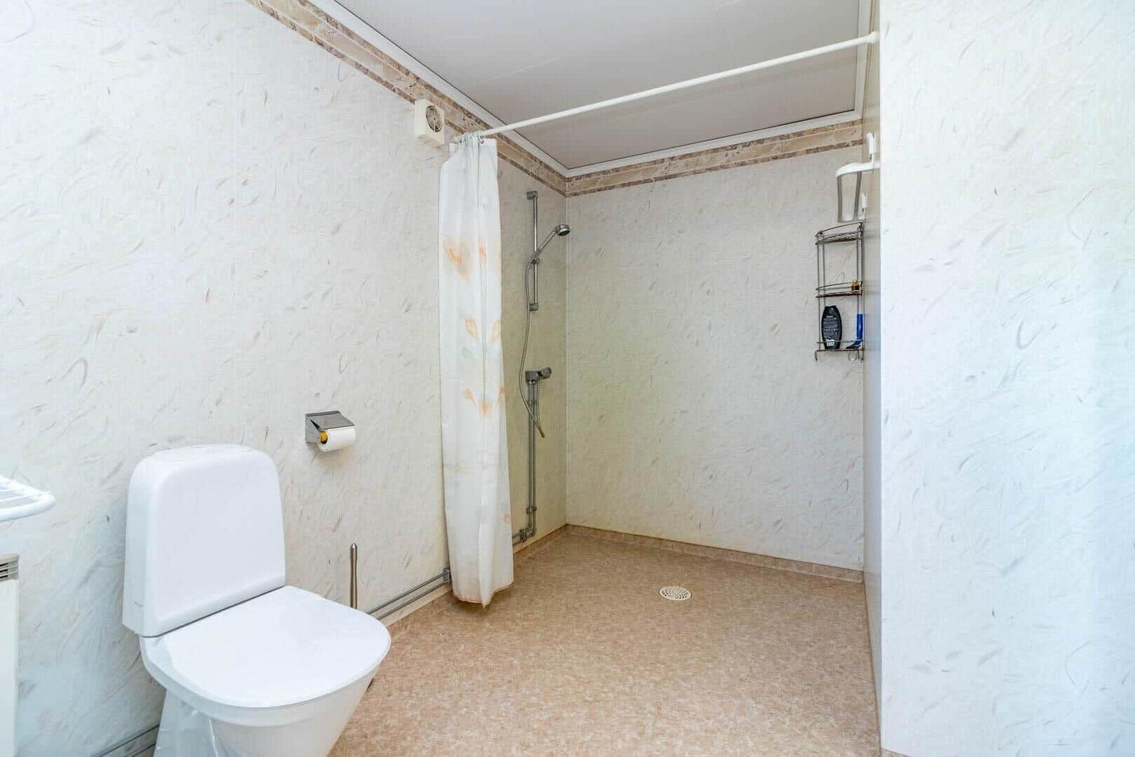 Bad mit Dusche, Toilette und Regal an der Wand.