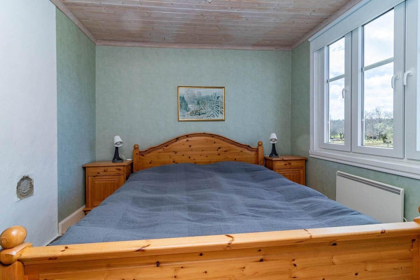 Schlafzimmer mit Holzbett, Nachttischen und Fenster mit Blick auf Landschaft.