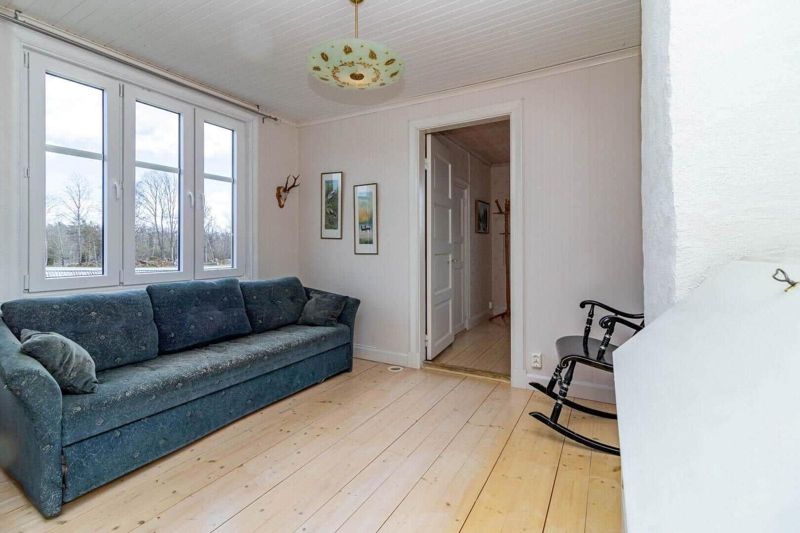 Ein Wohnzimmer mit blauem Sofa, Holzboden und großen Fenstern.