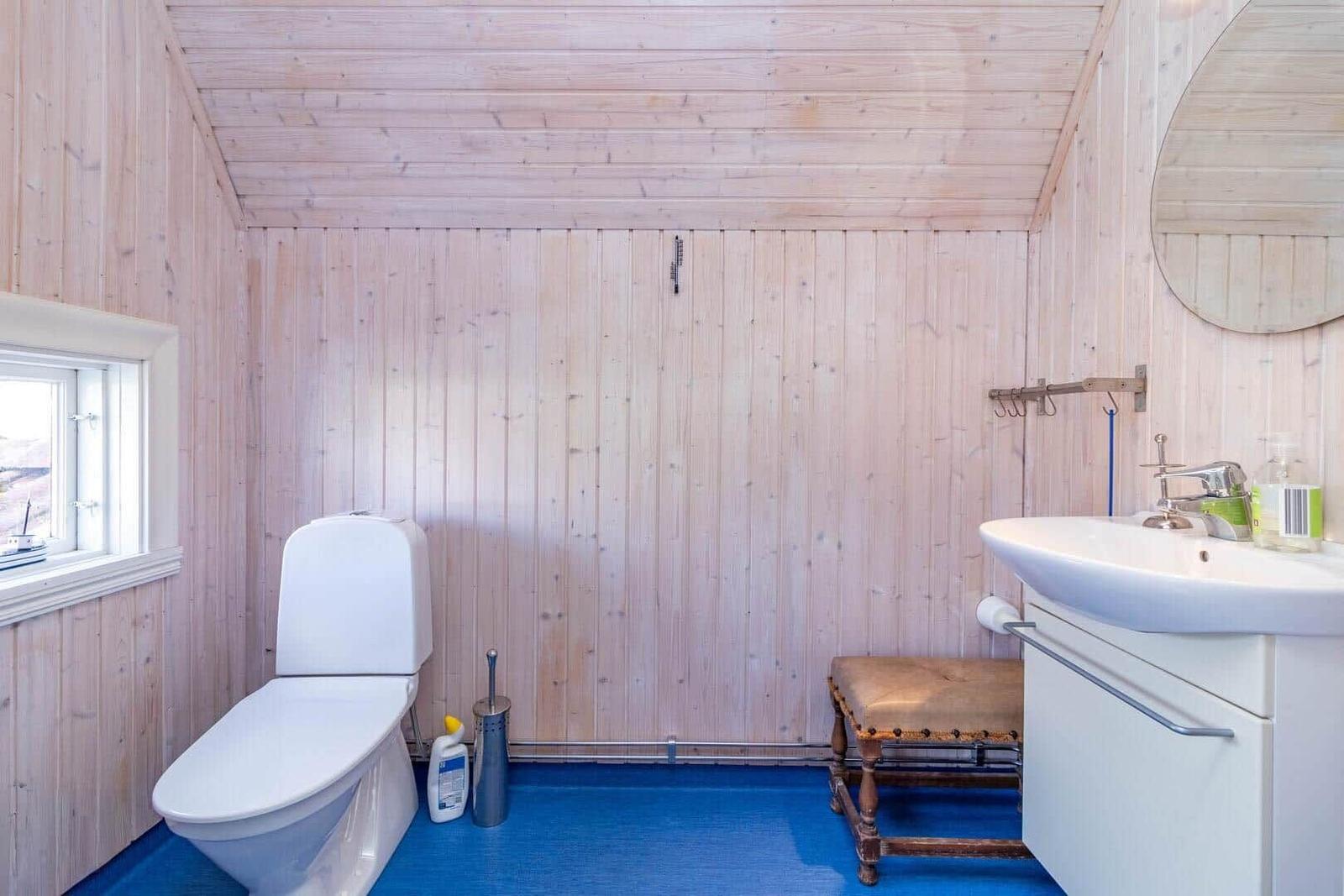 Badezimmer mit Holzwand, Toilette, Waschbecken und Fenster.