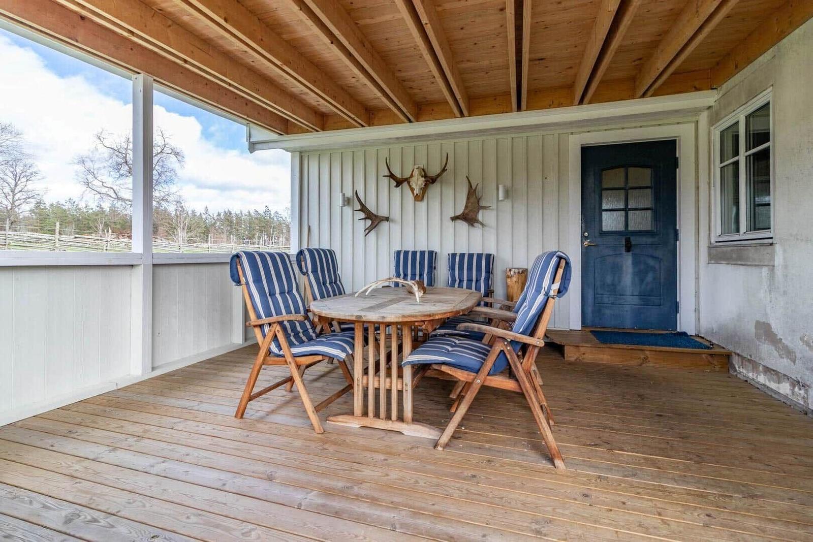 Terrasse mit Holztisch, sechs Stühlen und Hirschgeweih an der Wand.