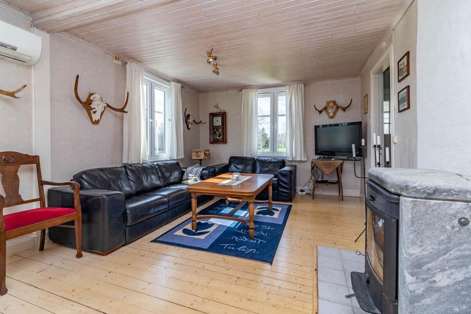 Wohnzimmer mit Ledersofa, Holztisch und Kaminofen. An den Wänden hängen Geweihdekorationen.