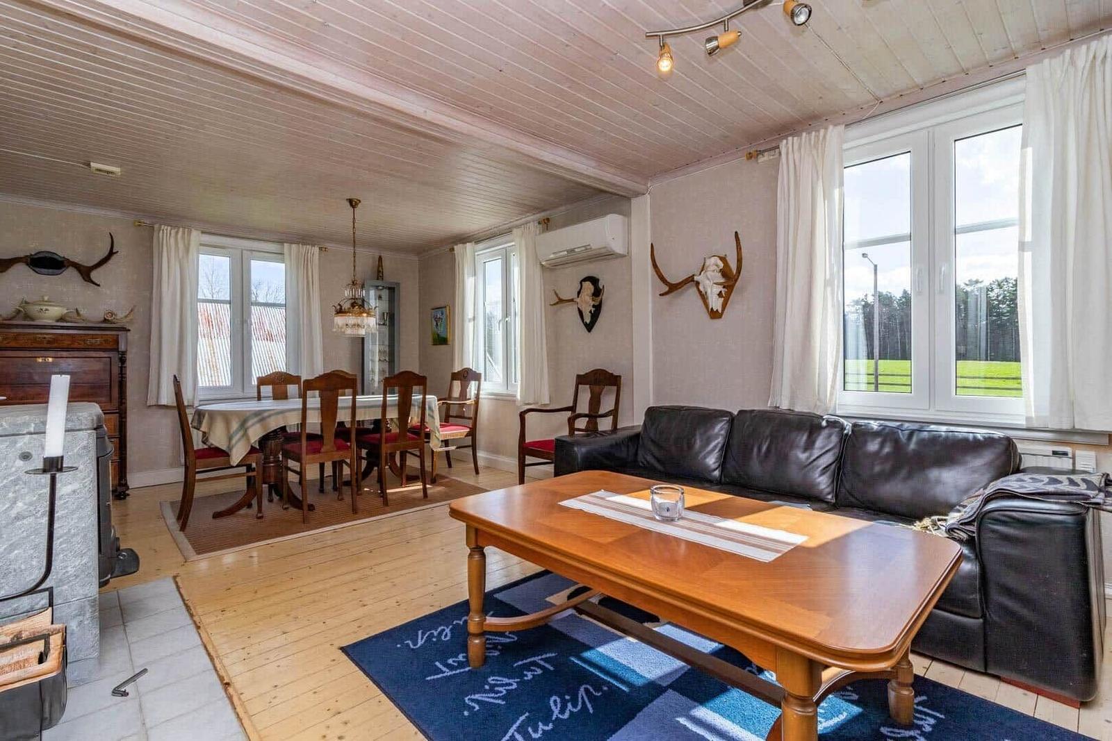 Wohn- und Essbereich mit Sofa, Esstisch und Holzboden. Fenster mit Blick auf Grünfläche.