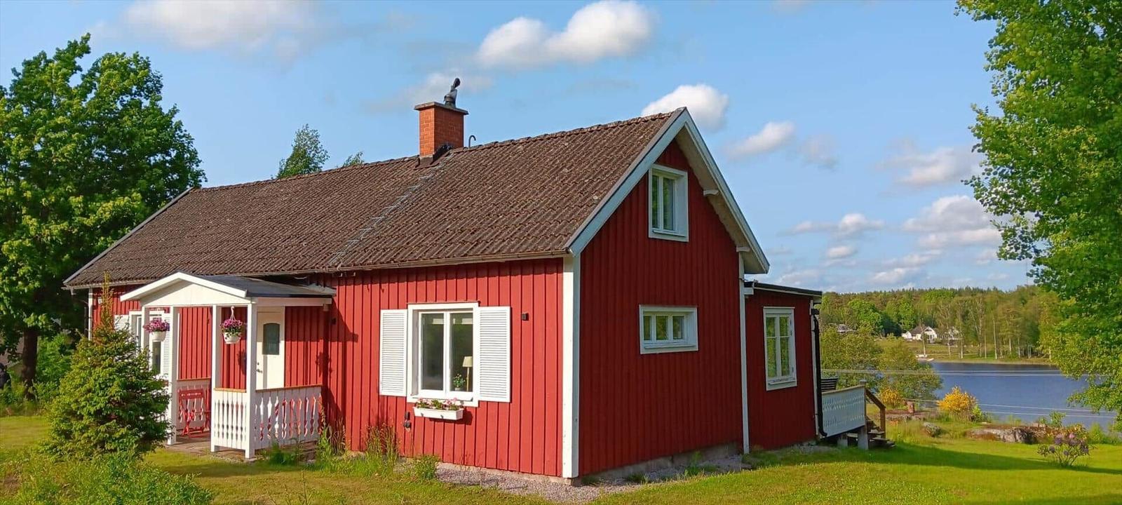 Rotes Holzhaus mit weißem Vordach und Blick auf einen See.
